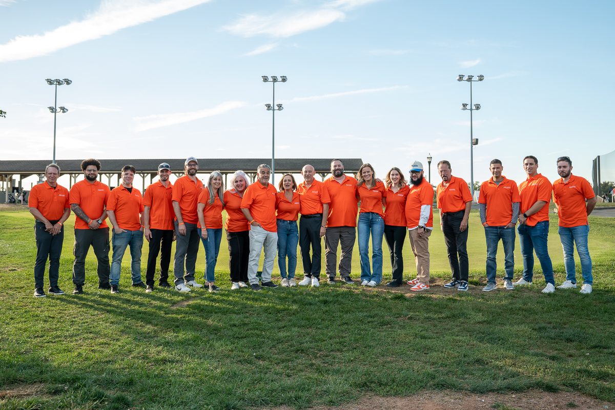Company team of about twenty people in matching orange polos lined up on a golf course lawn