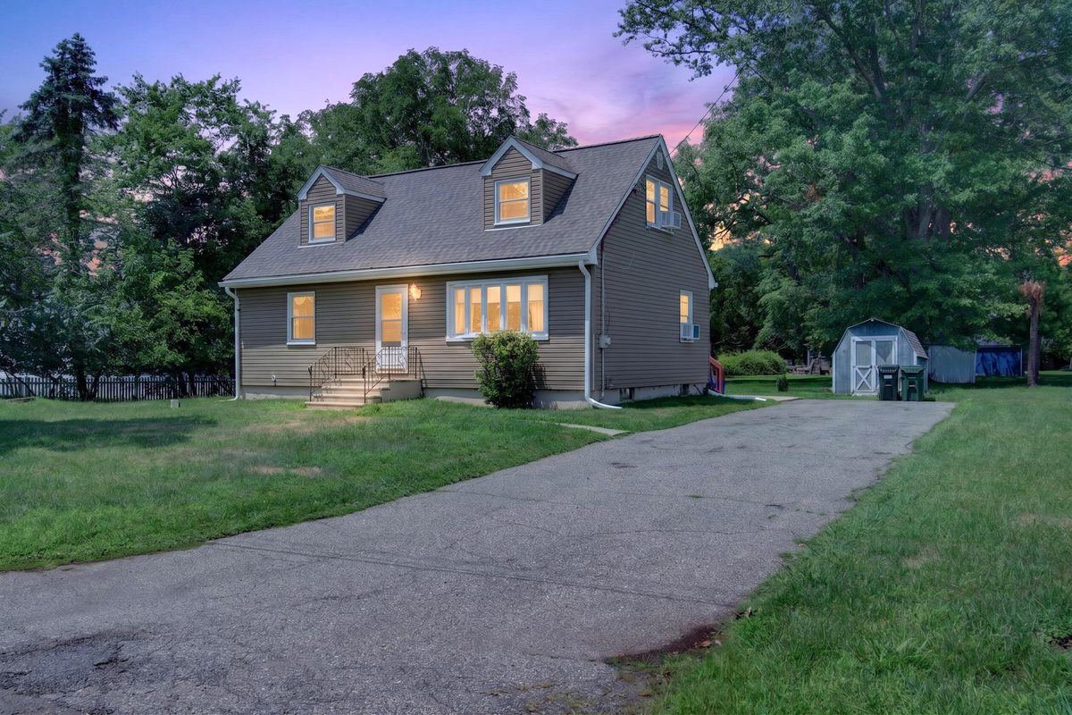 Twilight exterior of a Cape Cod style house with its windows lit